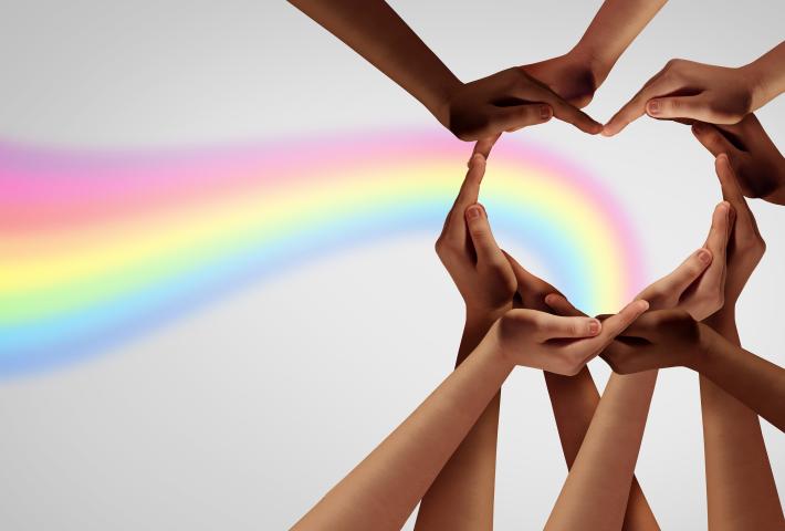 Diverse hands forming a heart with rainbow traveling through the hands